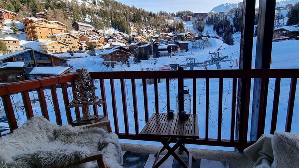 En balkon med udsigt over en snedækket landsby, træhuse og en skilift.