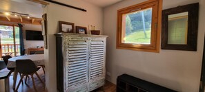 Ein Zimmer mit Holzschrank, Esstisch mit Stühlen, Fenster mit Blick ins Grüne und einer Bank.