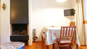 Ein Zimmer mit Kamin, Esstisch mit Stühlen, Wandfernseher und einem Fenster mit Vorhängen.