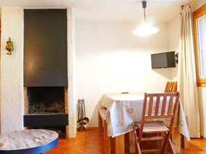 A room with a fireplace, a dining table with chairs, a television mounted on the wall, and a window with curtains. - 300m from ski slopes, 1st floor, terrace, fireplace or stove, tv, 40m², Montchavin La Plagne (Bellentre)