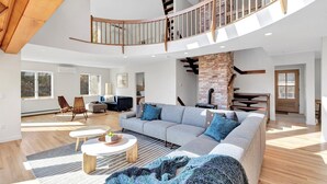 A spacious living area with a high ceiling, a built-in fireplace, and a curved staircase. - Modern 6 BR,5 B MarshViews,Hot tub,5mins to beach,Chef’s Kitchen, Large Groups (Barnstable)