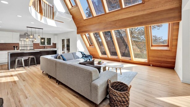 A spacious living area with a large sofa, a small coffee table, and a dining area with a kitchen in the background. - Modern 6 BR,5 B MarshViews,Hot tub,5mins to beach,Chef’s Kitchen, Large Groups (Barnstable)