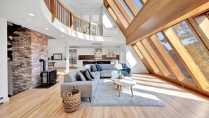 A spacious loft with a curved staircase, a cozy seating area, and a kitchen in the background. - Modern 6 BR,5 B MarshViews,Hot tub,5mins to beach,Chef’s Kitchen, Large Groups (Barnstable)