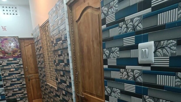 A hallway with patterned walls, a wooden door, and a striped rug. - JHARANA guest house (Puri)