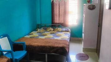 Un dormitorio con cama, una silla azul, ventilador de techo y una ventana con cortinas.