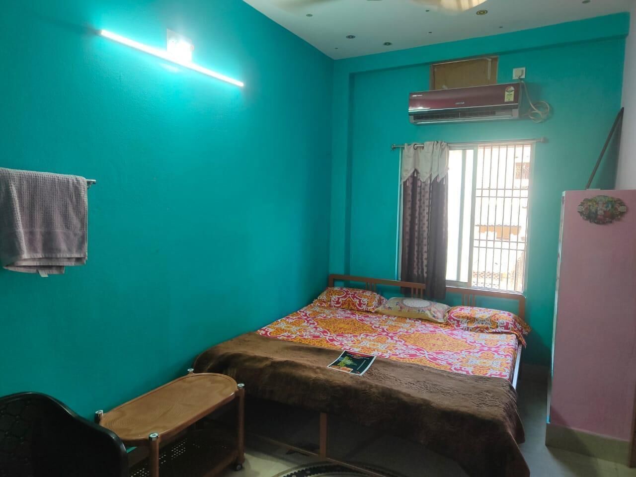 Een kleine kamer met een enkel bed, teal-kleurige muren, een houten bedframe, een bureau en een raam met tralies.