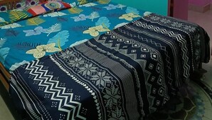 A bedroom with a floral-patterned wall, a bed with patterned bedspreads, and an air conditioning unit. - JHARANA guest house (Puri)