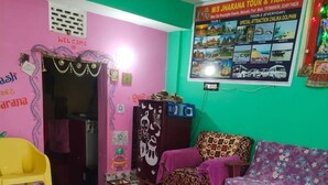 A room with a patterned floor, a sofa, a yellow chair, and a wall with a 'Welcome' sign and a poster advertising tours. - JHARANA guest house (Puri)