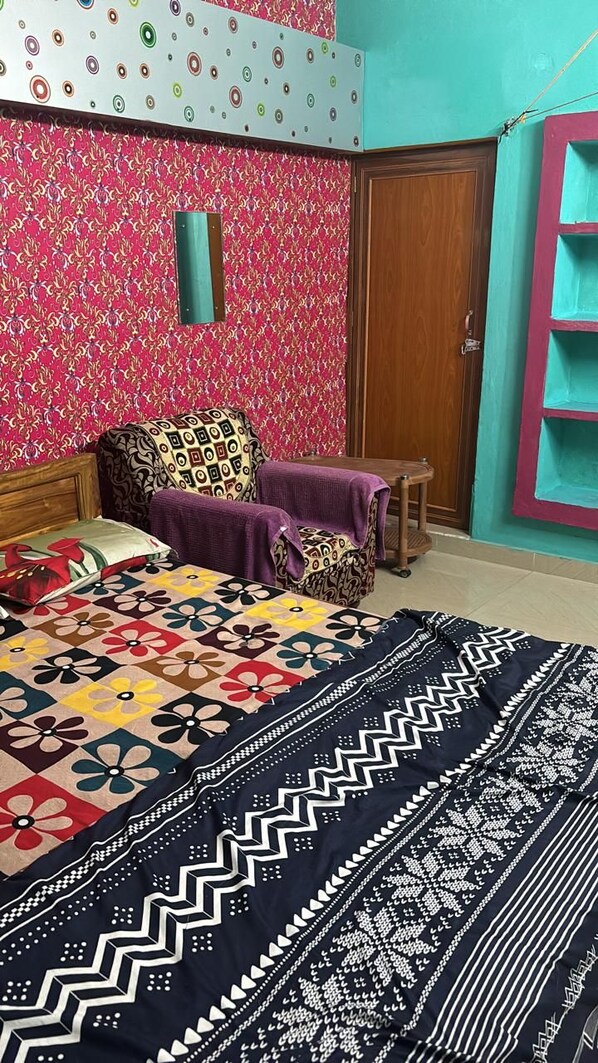 A bedroom with a patterned bedspread, a wooden headboard, a purple blanket, and a teal wall with a shelf. - JHARANA guest house (Puri)