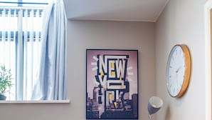Olohuoneessa on beige sohva, kaupunkimaisemaa esittävä juliste, kello ja lattiavalaisin.