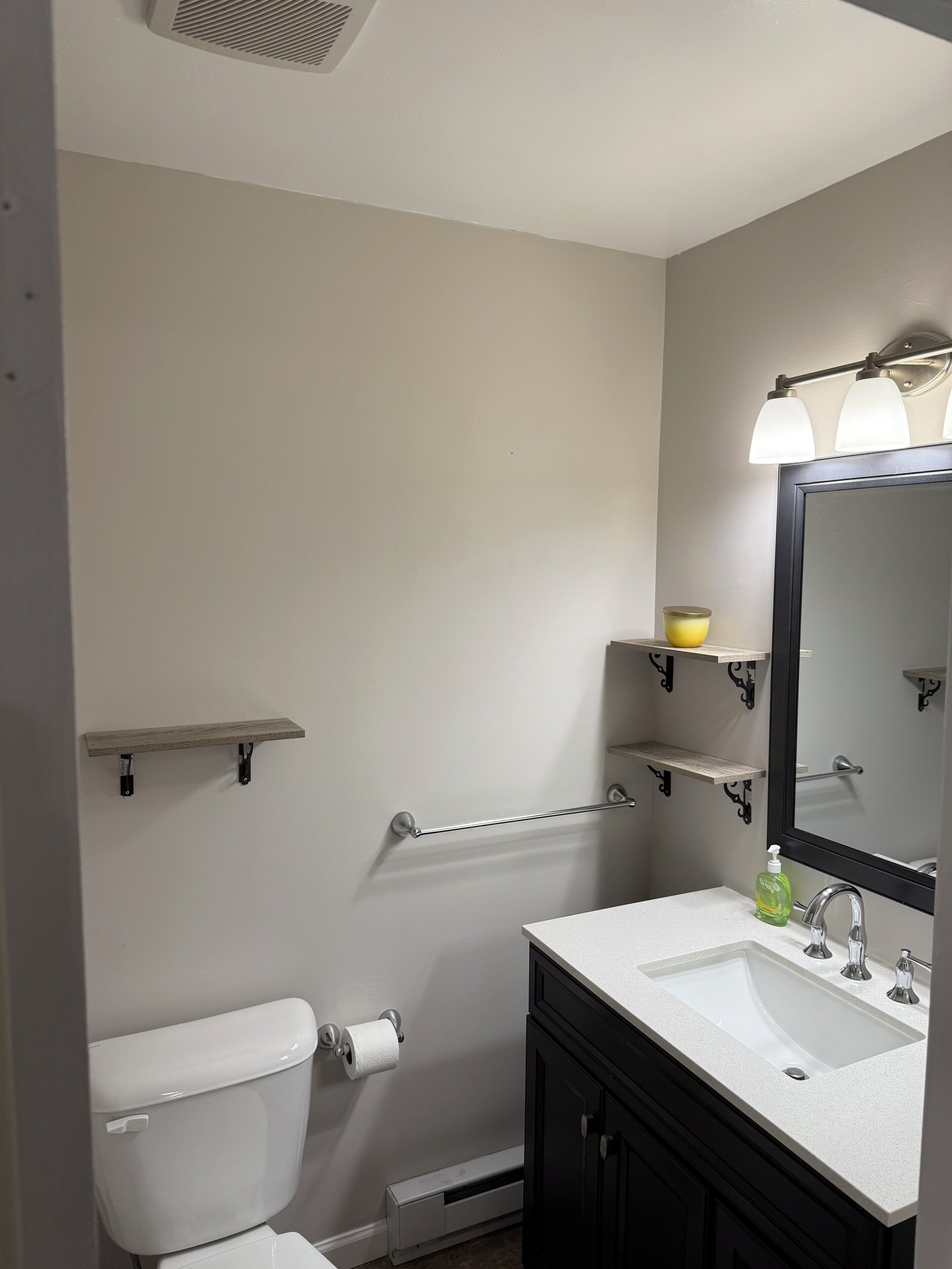 A bathroom with a toilet, sink, mirror, and shelves.