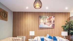 A modern living room with a wooden panel wall, a large painting, two sofas with blue and white cushions, a round coffee table, and two floor lamps. - Cosy Sheffield Cottage Retreat 2bedroom (Sheffield)