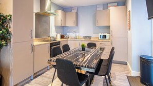 A modern kitchen with a marble countertop, black chairs, and a built-in oven. - Cosy Sheffield Cottage Retreat 2bedroom (Sheffield)