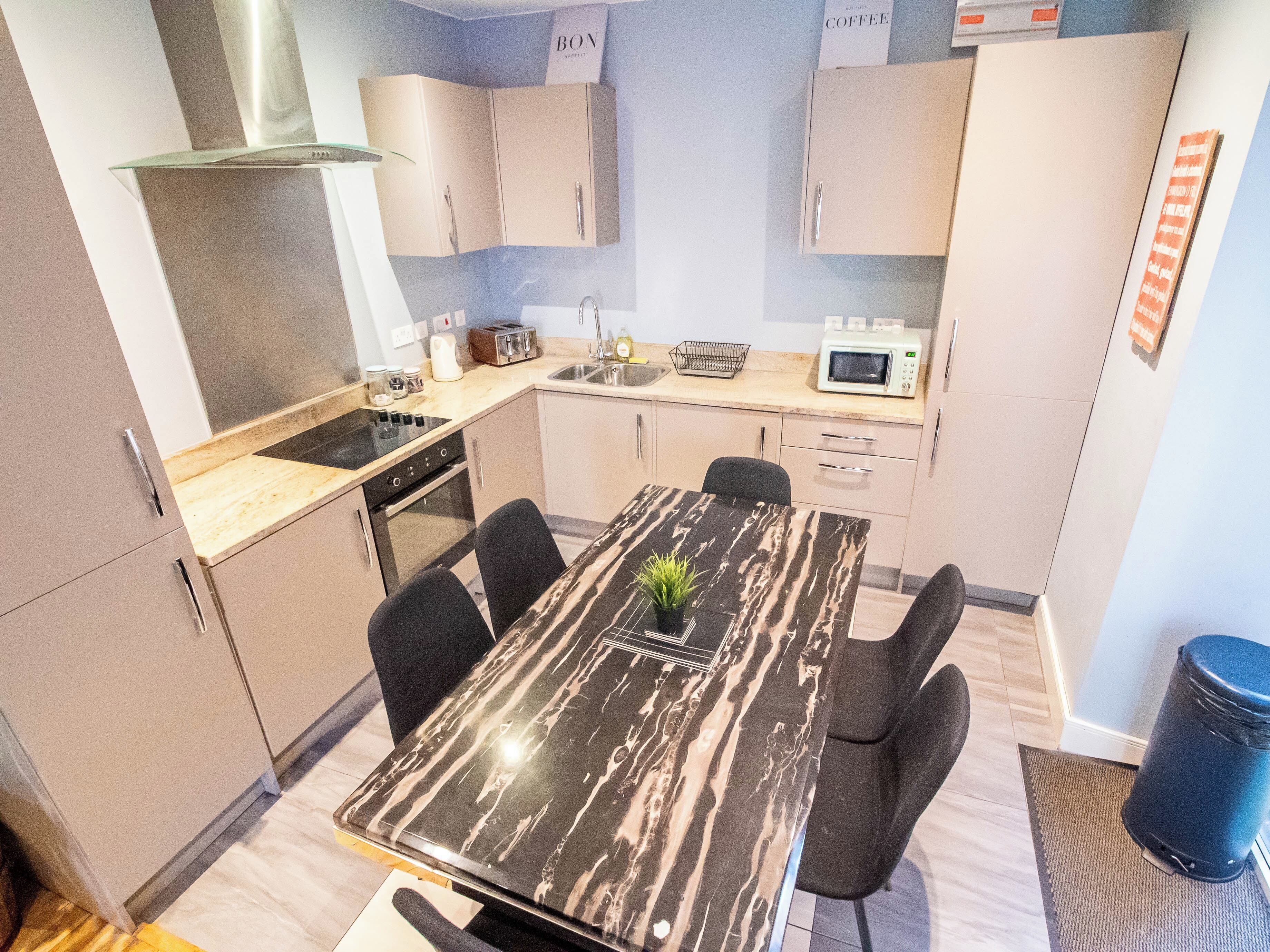 A modern kitchen with a marble table, black chairs, a microwave, and a sink.
