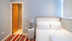 A bedroom with a bed, bedside table, lamp, and a door leading to a bathroom. - Cosy Sheffield Cottage Retreat 2bedroom (Sheffield)