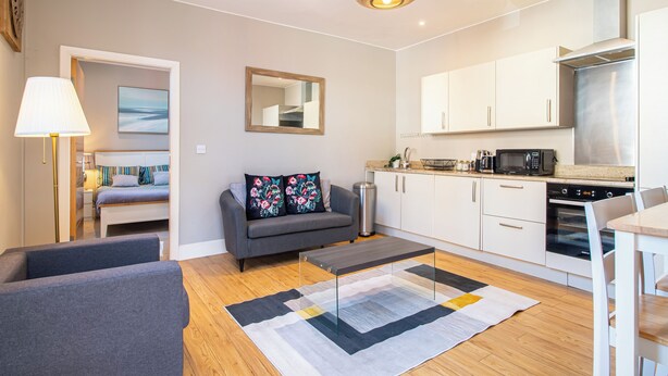 Un apartament modern amb saló, sofà, taula de centre, zona de cuina amb armaris i electrodomèstics, i taula de menjador.