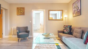 A modern living room with a grey armchair, a sofa, a glass coffee table, and a decorative bowl. - Cozy 2bedroom Sheffield City Apartment (Sheffield)