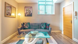 A living room with a sofa, a glass coffee table, and a large window with blinds. - Cozy 2bedroom Sheffield City Apartment (Sheffield)