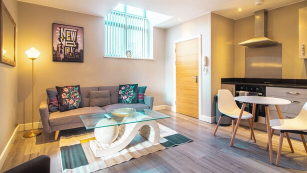 A modern living room with a glass coffee table, a sofa with decorative pillows, a dining area with a white table and chairs, and a kitchen with a stove and cabinets. - Cozy 2bedroom Sheffield City Apartment (Sheffield)