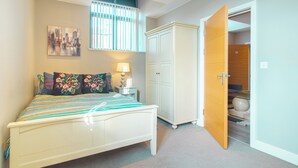 A bedroom with a bed, a nightstand, a lamp, a wardrobe, and a door leading to another room. - Cozy 2bedroom Sheffield City Apartment (Sheffield)