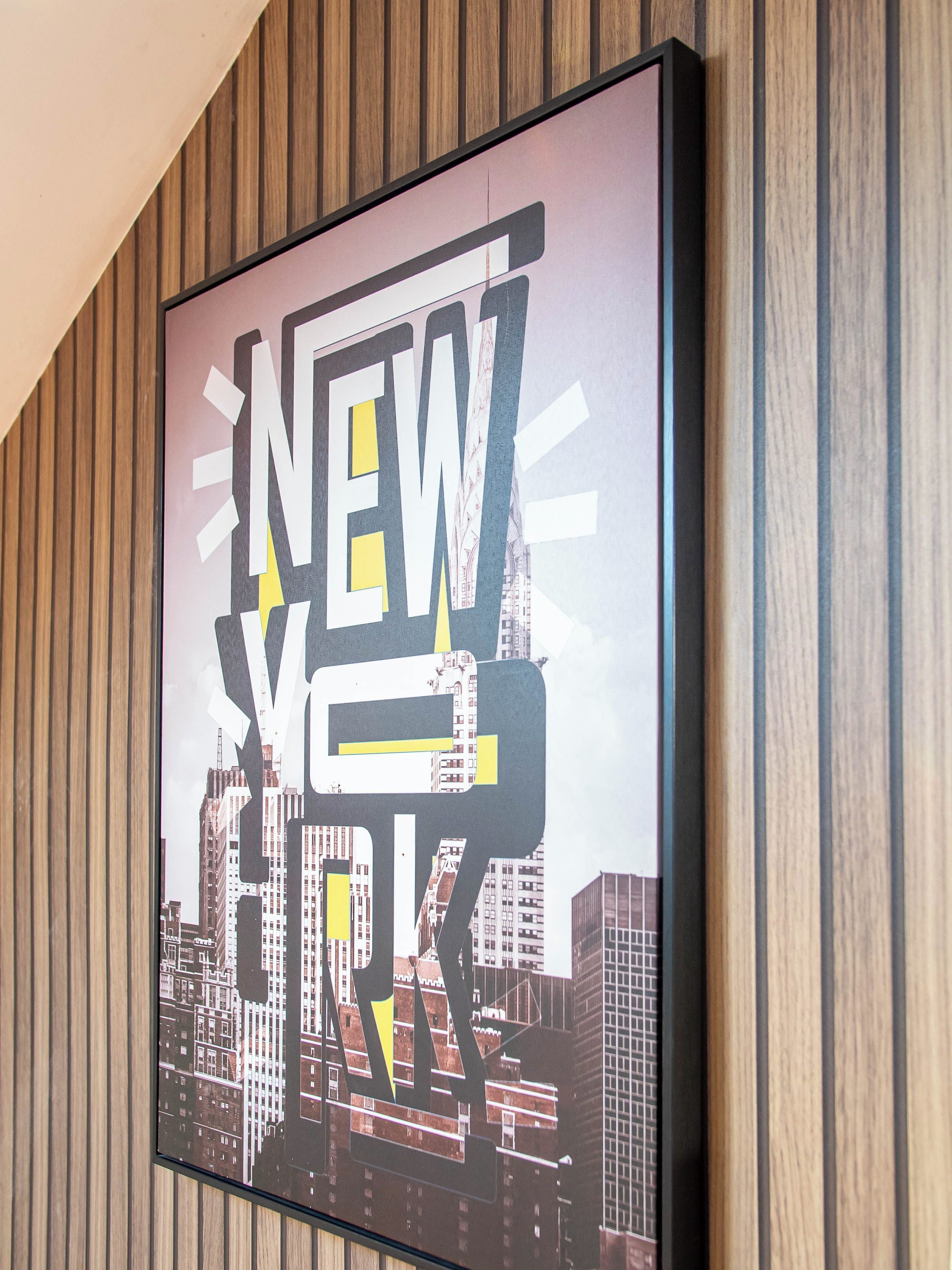 Une œuvre d’art encadrée, portant l’inscription « NEW YORK » et illustrant un paysage urbain.