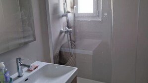 Een badkamer met een wit wastafelmeubel, een spiegel en een douchegedeelte.