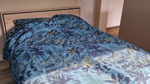 Een bed met een bloemenprintdeken in een kamer met houten vloeren en een effen muur.