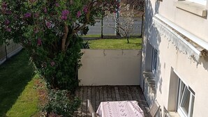 Een houten terras met een tafel en stoelen, omgeven door groen en een gebouw.