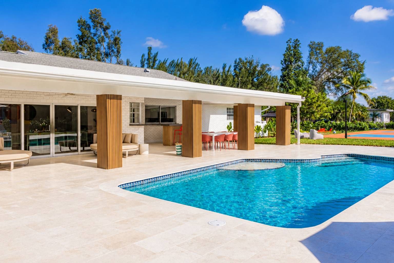 A modern outdoor swimming pool area with a covered patio, seating, and a view of the surrounding landscape.