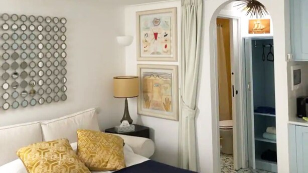 A hotel room with a bed, a mirror wall, artwork, and a bathroom visible through an open door. - Villa Sain Charming Suite (Anacapri)