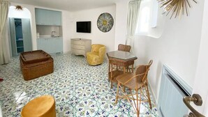 A room with a dining table, chairs, a television, a decorative wall piece, and a window with curtains. - Villa Sain Charming Suite (Anacapri)