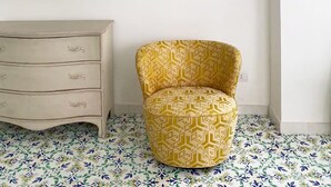 A room with a flat-screen TV mounted on the wall, a patterned yellow armchair, a white dresser, and a decorative circular mosaic on the wall. - Villa Sain Charming Suite (Anacapri)
