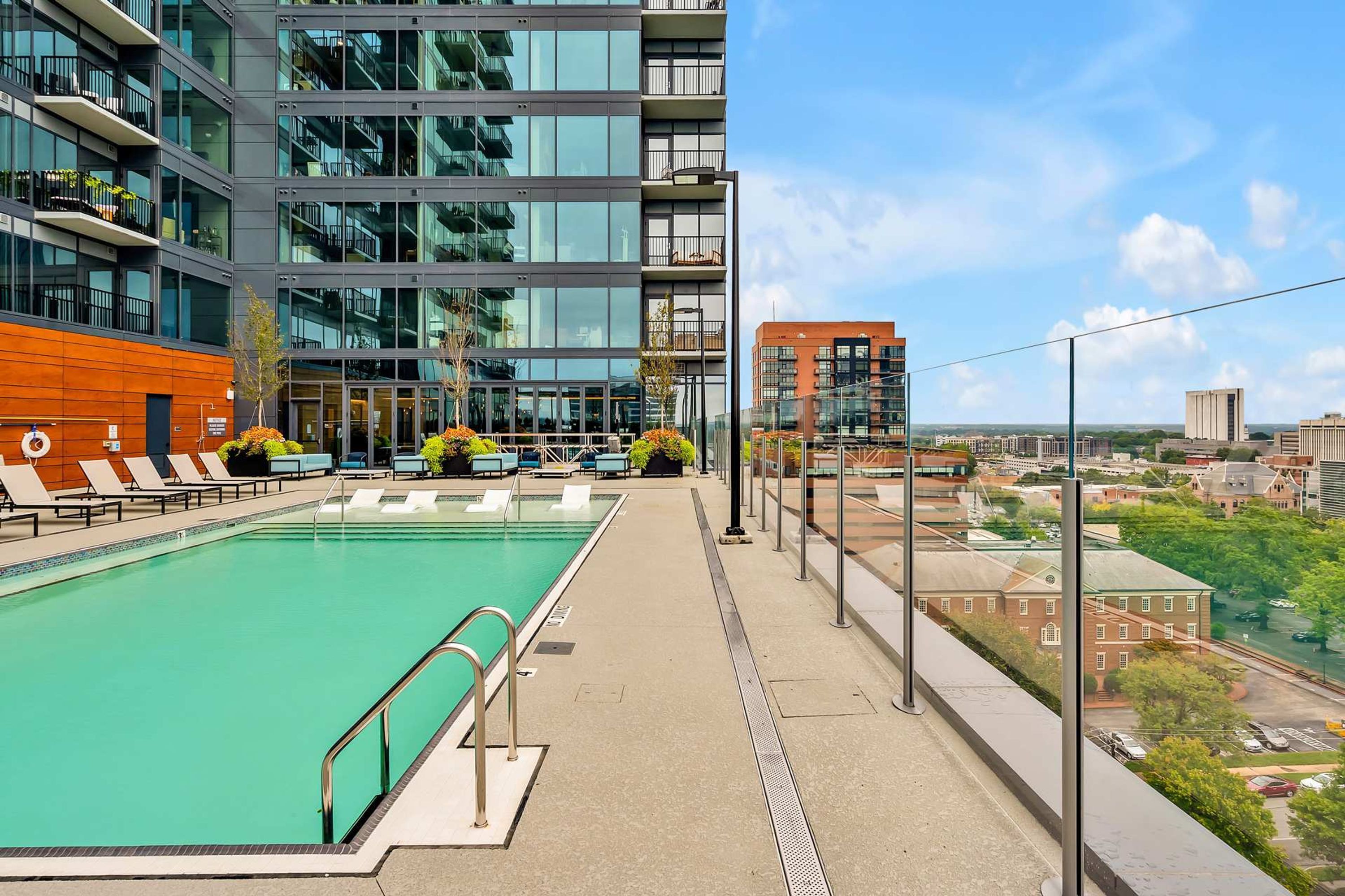A modern building with a rooftop pool, lounge chairs, and a view of the city.