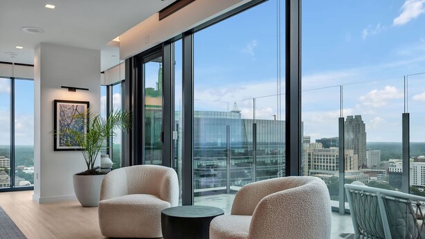 Een moderne hotelkamer met grote ramen, twee comfortabele fauteuils, een klein rond tafeltje en een kamerplant.