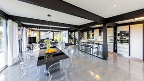 A spacious kitchen with modern appliances, a dining area with clear chairs, and a large window providing natural light. - Villa Leonardo (Gebhardshain)