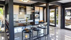 A modern kitchen with a central island, bar stools, and large windows. - Villa Leonardo (Gebhardshain)