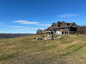 A two-story house with a covered porch, a large deck, and a view of the surrounding hills.