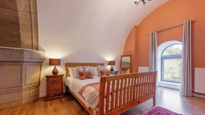 Un dormitorio con cama de madera, dos mesitas de noche con lámparas, un ventanal con cortinas y vistas al exterior.