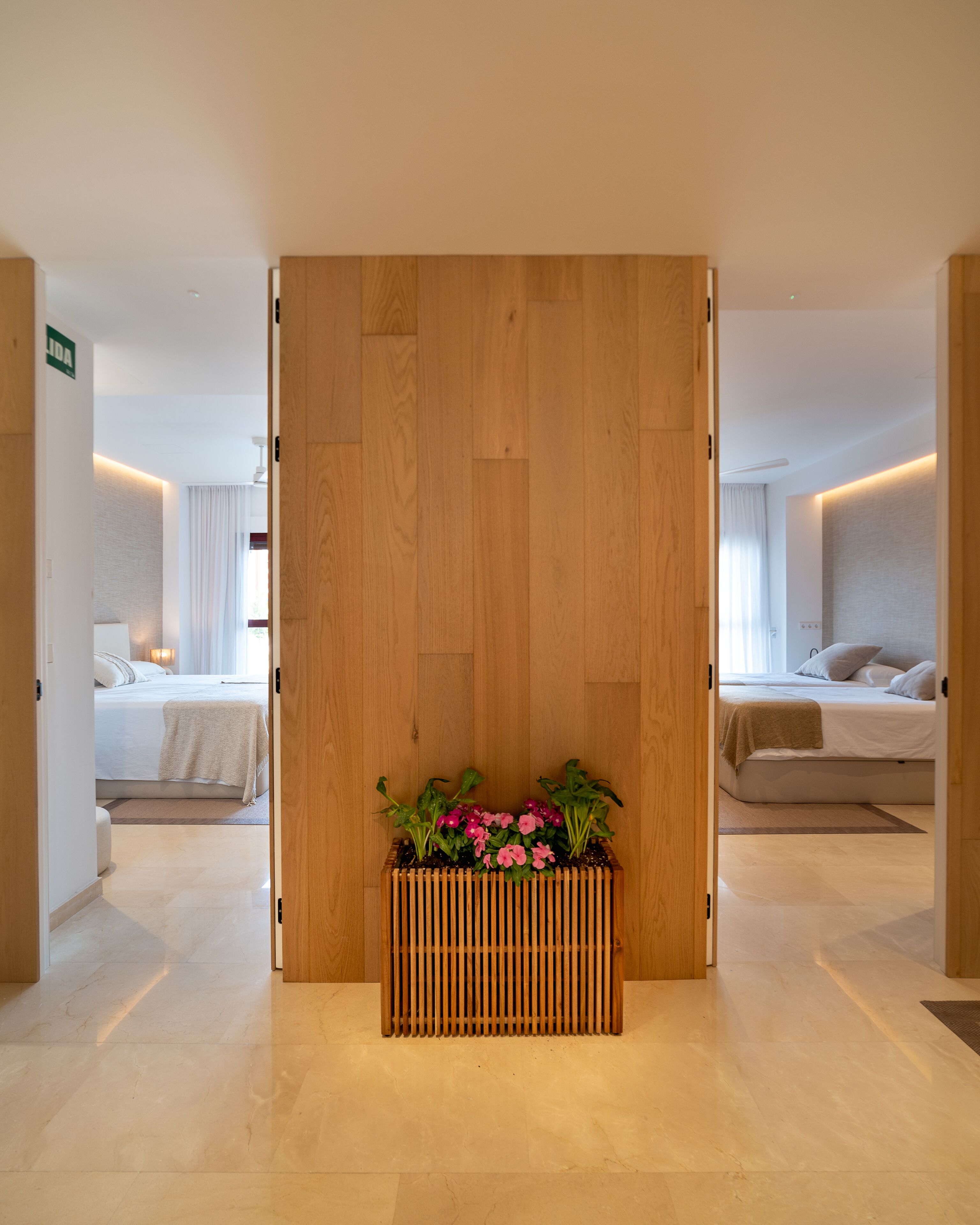 Een hotelkamer met een houten scheidingswand, een bed, een nachtkastje en een bloeiende plant in pot.