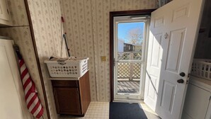 Una habitación con un armario de madera, un cesto de ropa, una bandera a rayas y una puerta que da a un balcón.