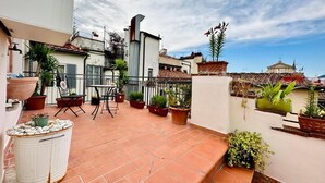 A rooftop terrace with terracotta tiles, potted plants, a table and chairs, and a white trash bin. - Terrace Studio   Apartment with panoramic terrace (Florence)