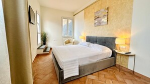 A bedroom with a large bed, a bedside table with a lamp, a chair, and a window with shutters. - Terrace Studio   Apartment with panoramic terrace (Florence)