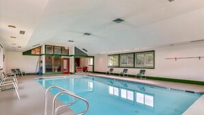 Ein Swimmingpool mit klarem, blauem Wasser, umgeben von Liegestühlen und einem kleinen Gebäude mit roter Tür.