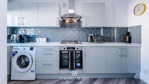 Une cuisine moderne avec des meubles blancs, un four encastré, un lave-linge et une machine à café.