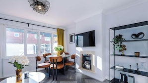 Un salon moderne avec une cheminée, un coin repas avec des chaises, un téléviseur fixé au mur et une bibliothèque.