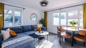 Un salon moderne avec un canapé bleu, une table basse ronde et un coin repas avec des chaises.
