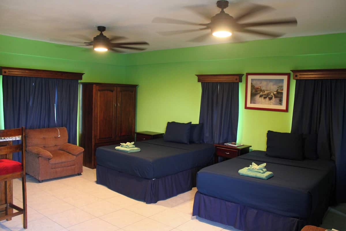 Habitación de hotel con dos camas, una silla, un escritorio y un ventilador de techo.