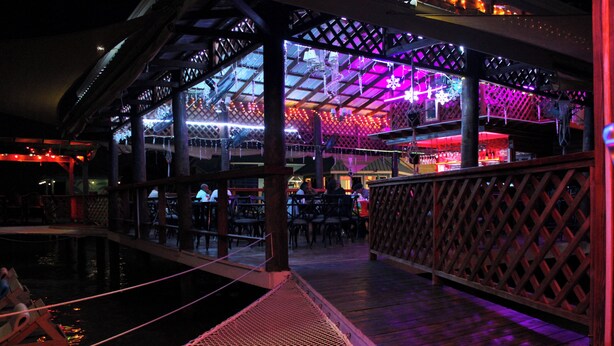 Zona de bar interior con piscina, terraza de madera y techo con celosía.
