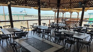 Un restaurante frente a la playa con terraza, mesas y sillas.