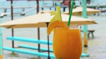 A tropical drink with a straw and garnish on a wooden table, with a pool and umbrellas in the background.